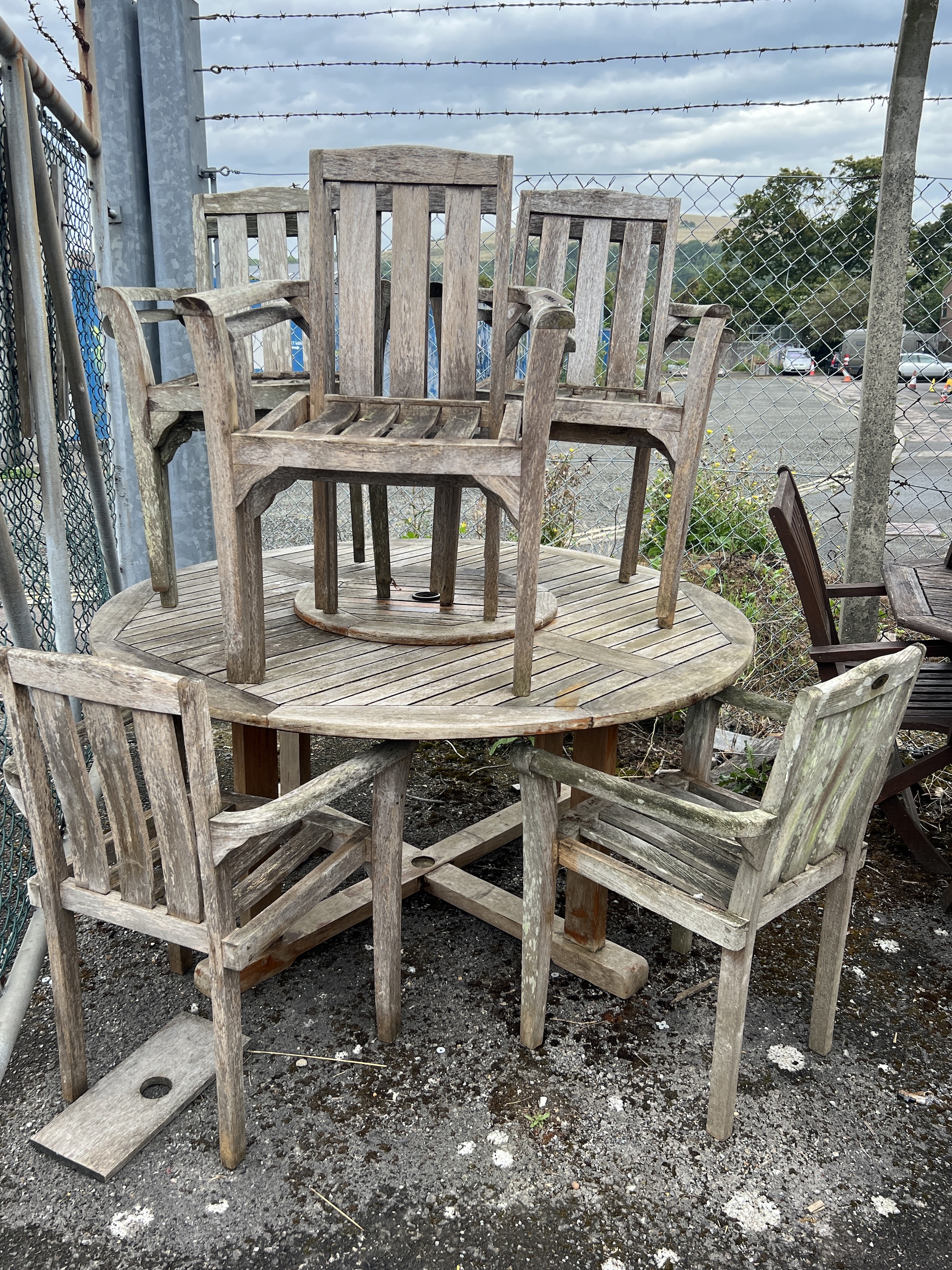 A circular weathered teak garden table with 'Lazy Susan' diameter 150cm, width 85cm, height 71cm and eight elbow chairs